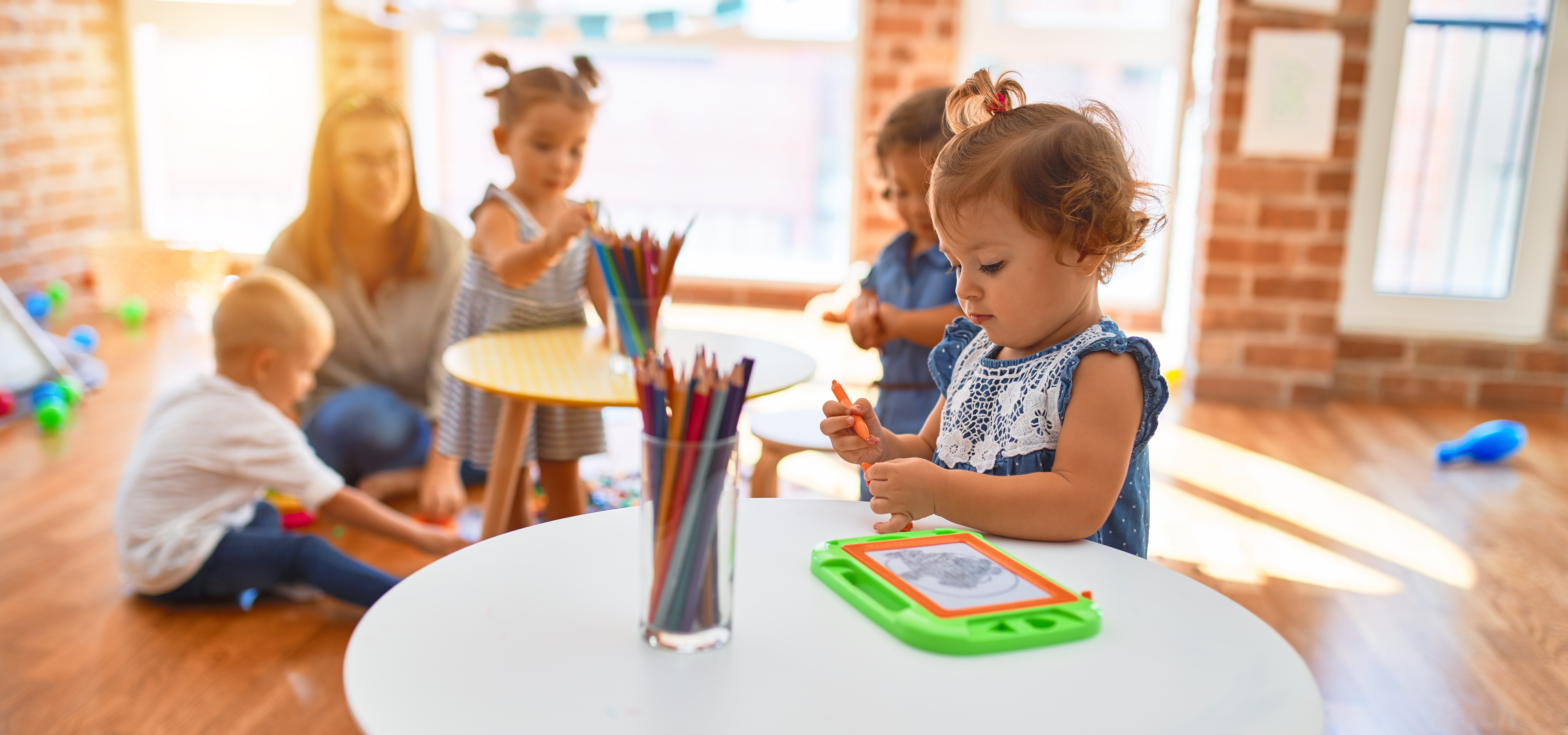 Beautiful teacher and group of toddlers playing around lots of toys at kindergarten